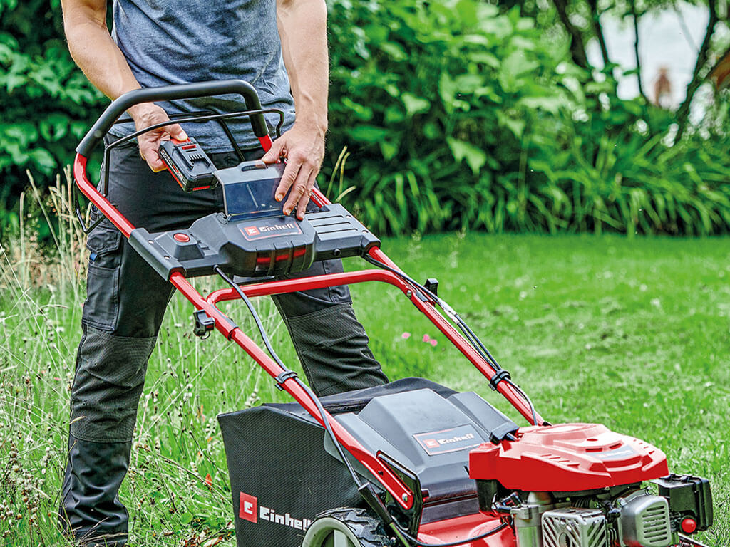 A man puts the battery into the lawn mower