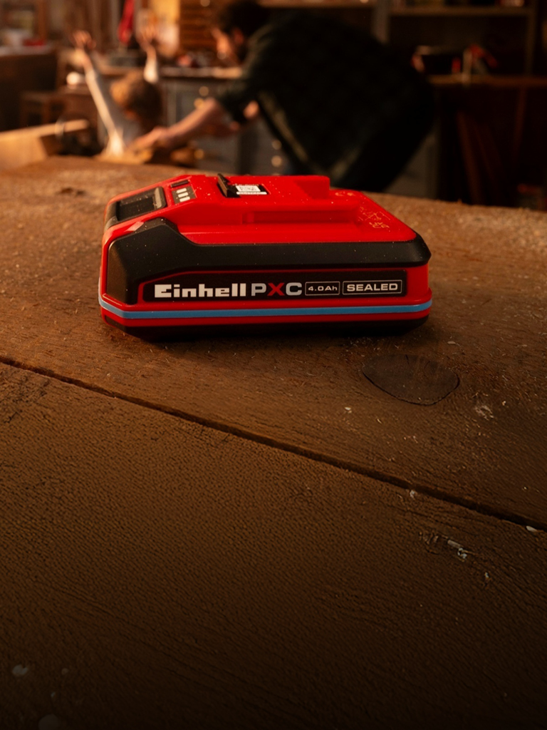 Einhell Power X-Change 4.0Ah SEALEAD battery on a wooden workbench, showing blue ring and label.