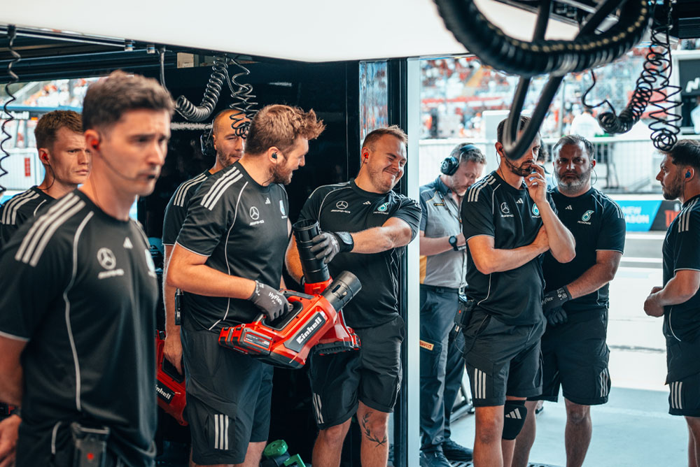 Das Mercedes-AMG PETRONAS Formula One Team befindet sich in der Garage. Zwei Teammitglieder halten rote kabellose Gebläse von Einhell und bereiten sich auf die nächste Aktion vor.