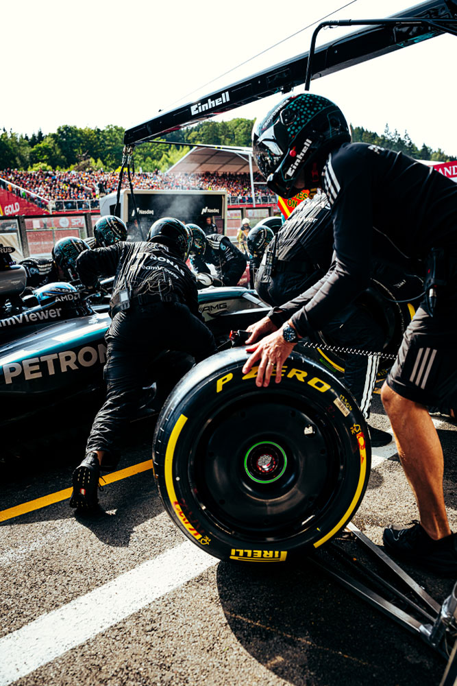 Mechaniker des Mercedes-AMG PETRONAS Formula One Teams führen einen Boxenstopp durch. Ein Teammitglied bereitet einen Pirelli-Reifen vor, während andere am Auto arbeiten. Das Einhell-Branding ist auf der Ausrüstung über dem Auto sichtbar.