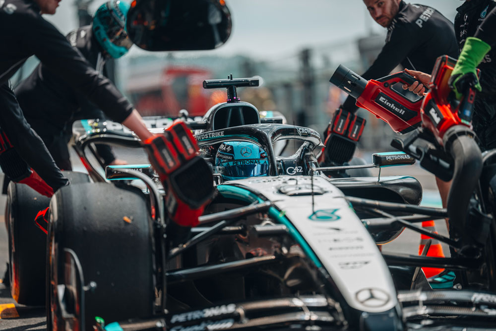 Ein Mercedes-AMG PETRONAS Formula One Wagen während eines Boxenstopps. Teammitglieder verwenden kabellose Gebläse von Einhell, um Fahrzeugkomponenten zu kühlen. Das Team arbeitet konzentriert und präzise.