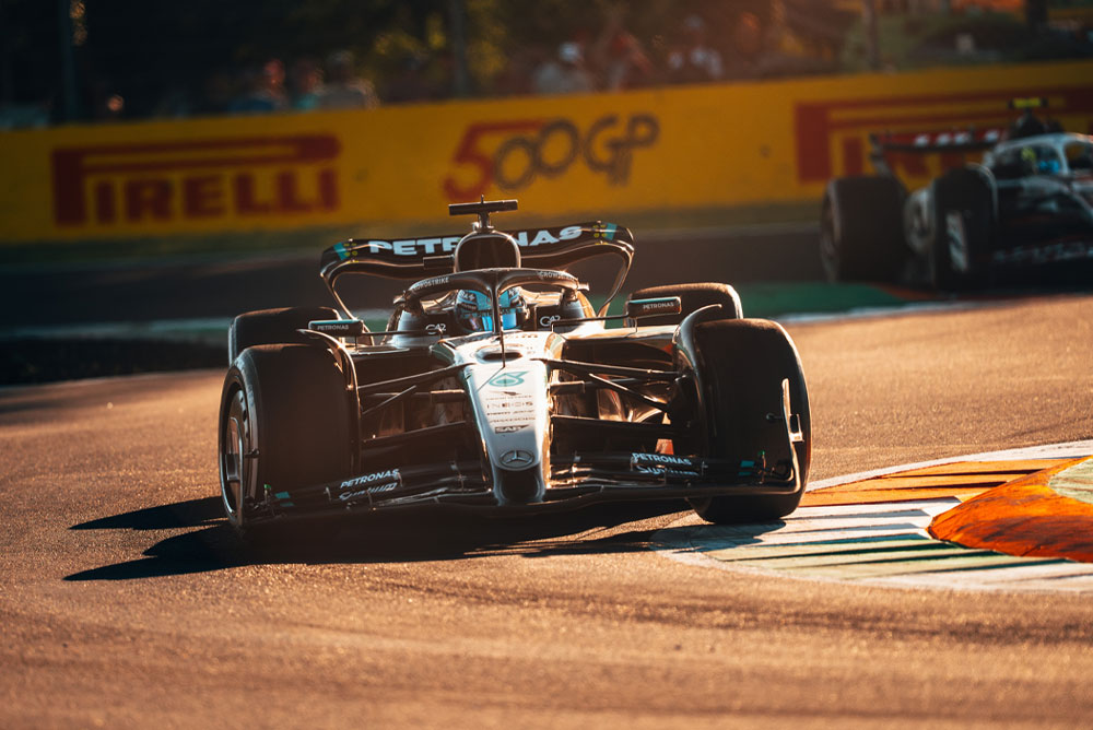 Ein Mercedes-AMG PETRONAS Formula One Wagen fährt während eines Grand Prix auf einer sonnendurchfluteten Strecke. Das Auto nimmt mit hoher Geschwindigkeit eine Kurve, während ein weiteres Fahrzeug im Hintergrund zu sehen ist.