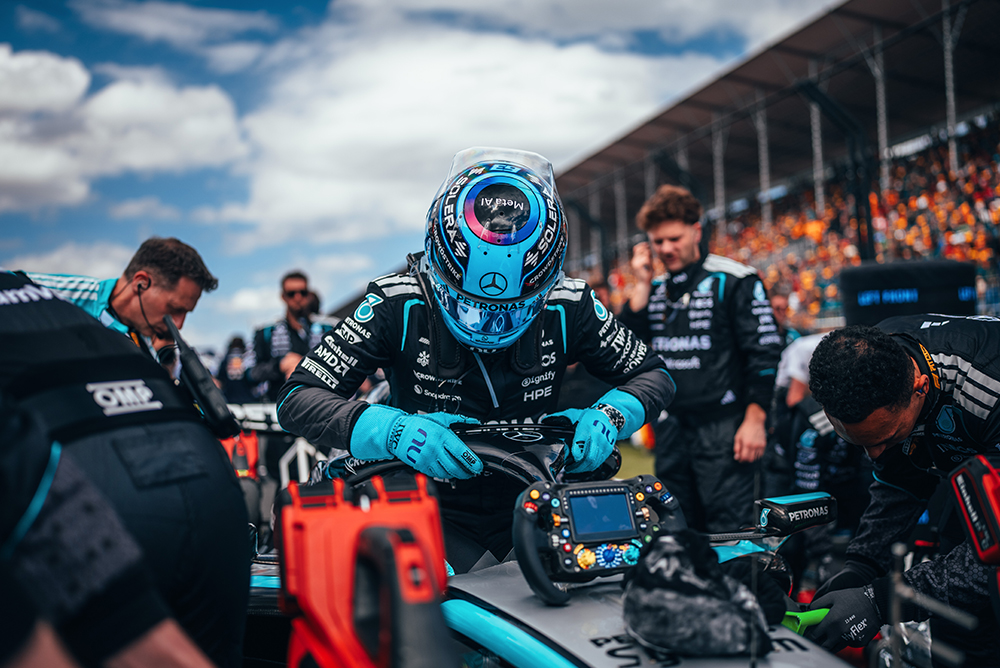 Formel-1-Fahrer sitzt im Rennwagen, umgeben vom Team auf der Startaufstellung.