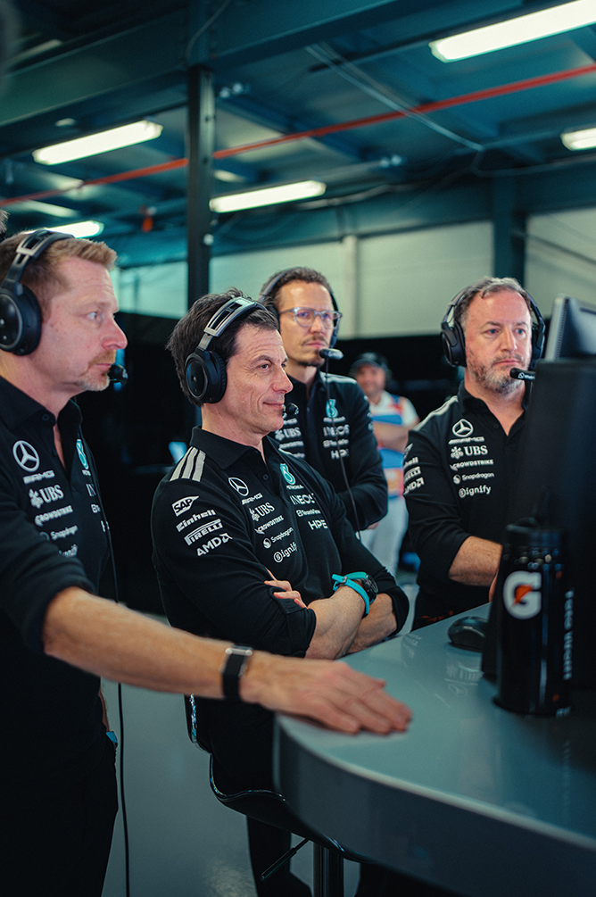 Formel-1-Teammitglieder mit Headsets verfolgen das Rennen von der Boxenmauer.