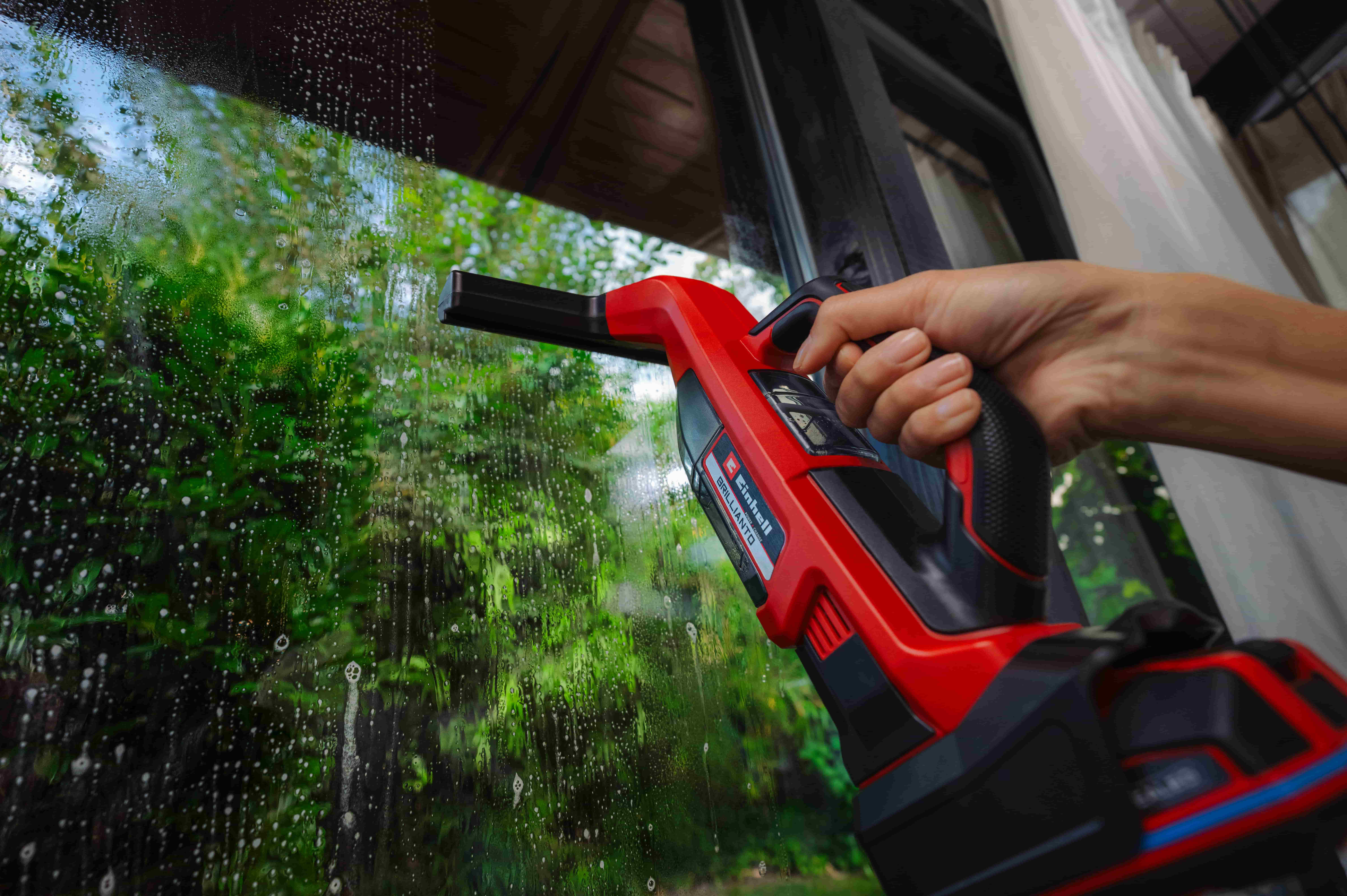 Hand cleaning a window with an Einhell cordless pressure washer.