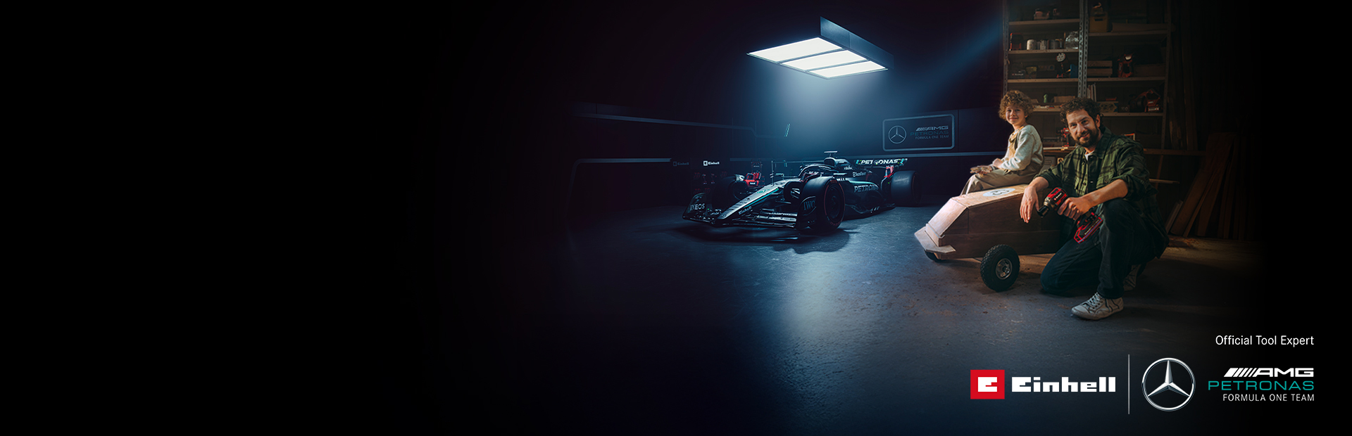 Ein Vater und Kind sind in einer Werkstatt mit einem selbstgebauten Seifenkistenauto. Im Hintergrund ein Mercedes-AMG PETRONAS Formel-1-Wagen und Einhell-Werkzeuge.