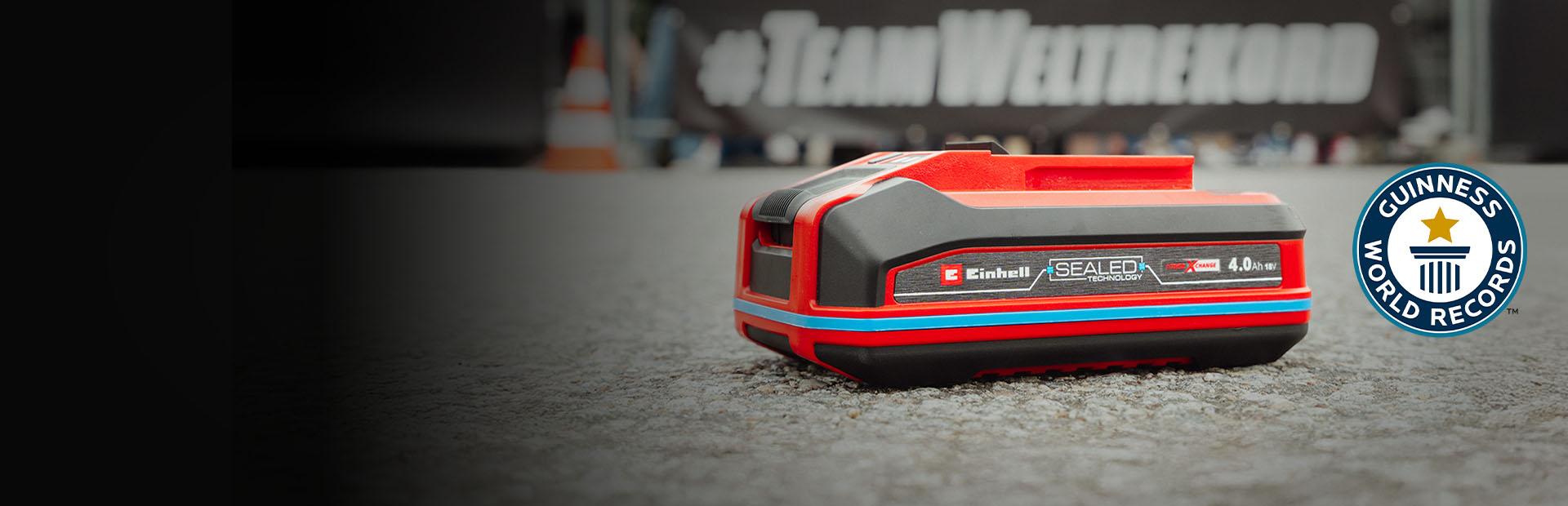 Einhell SEALED battery Power X-Change 4.0 Ah lies on asphalt, with the Guinness World Records "Record Holder" logo on the right.