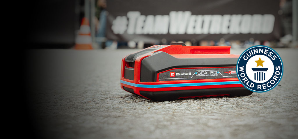 Einhell SEALED battery Power X-Change 4.0 Ah lies on asphalt, with the Guinness World Records "Record Holder" logo on the right.