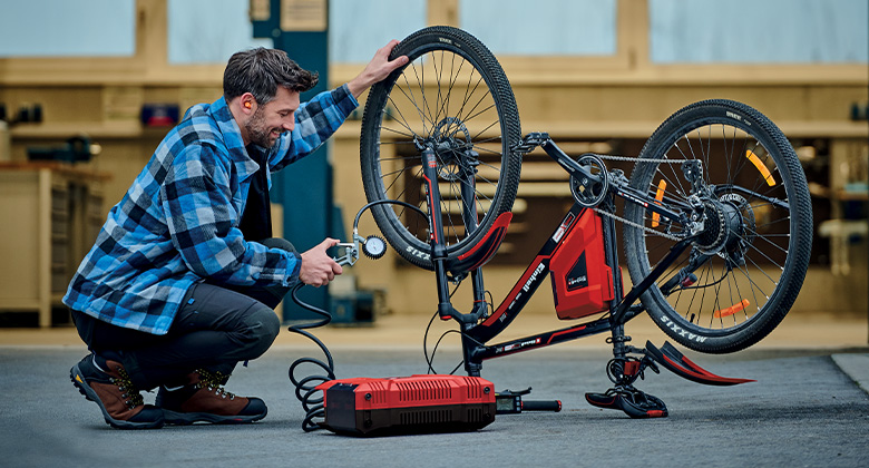 Ein Mann nutzt einen Einhell-Kompressor, um ein Fahrrad in einer Werkstatt aufzupumpen.